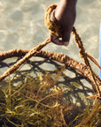 Close up view of a hand holding a basket of harvested seaweed in the ocean.