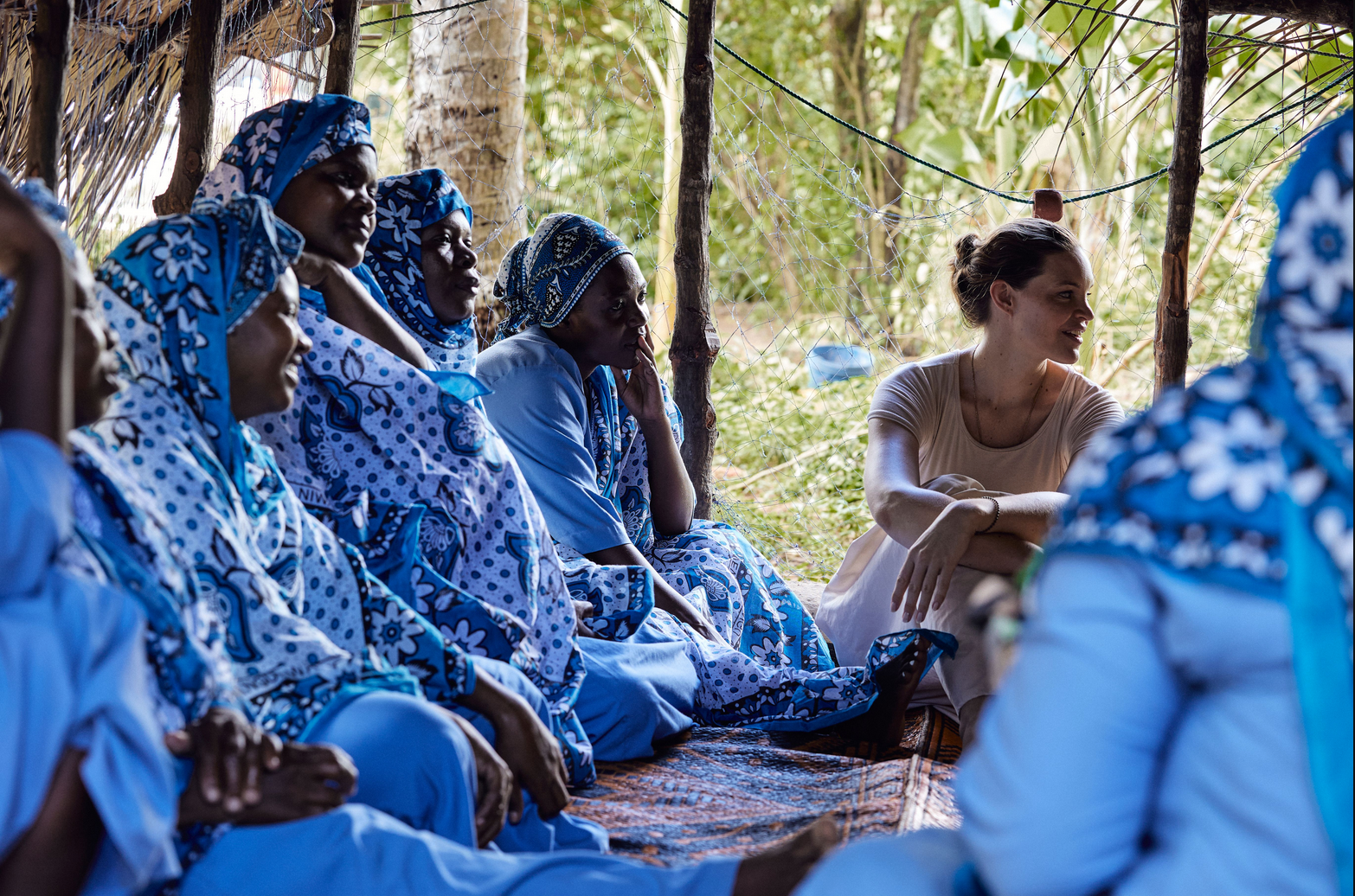Several Mwani Zanzibar Mamas and an a Mwani Zanzibar co-founder seated together on a floor in conversation.